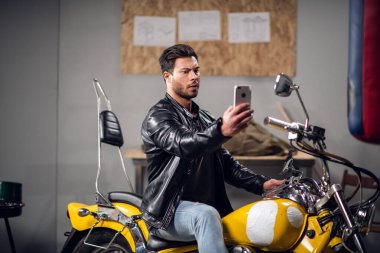Sarı havalı motosikletli şık bir adam garajda ya da araba tamirhanesinde selfie çekiyor.