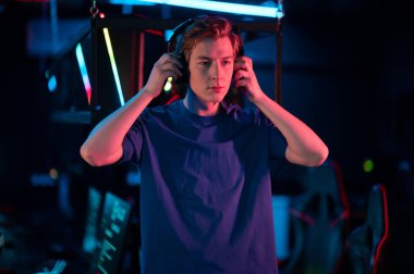 Sevimli genç bir oyuncu bilgisayar odasında kafasına kulaklık takıyor.