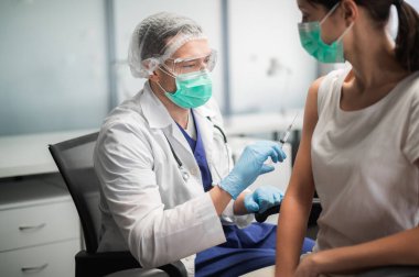 Genç bir tıp öğrencisi genç bir kızın omzuna koronavirüs aşısı enjekte ediyor.