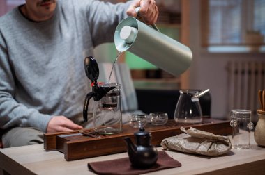 Geleneksel Çin törenlerinin gerçek bir ustası çaydanlığa sıcak su dökerek çiğ siyah çay demler. Evde konforlu çay partisi.