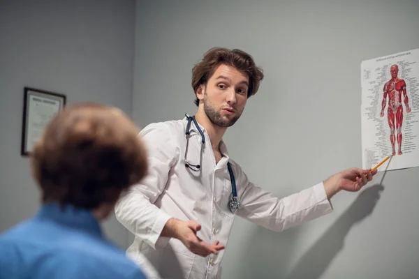 Young doctor explaining things to his patient, the patient is blurred, sitting in the foreground