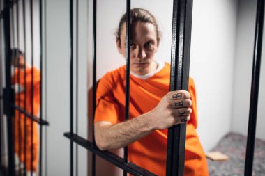 Hücrede dövmeleri olan umutsuz bir suçlu demir parmaklıklar ardında tutuluyor. Kameraya dikkatlice bak..