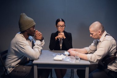 Siyahi bir uyuşturucu bağımlısı, deneyimli bir müfettiş ve devlet avukatı tarafından karakolda sorgulanır.