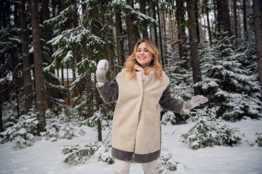 Kış ormanında kürk giymiş güzel bir sarışın ailesiyle kartopu oynuyor.