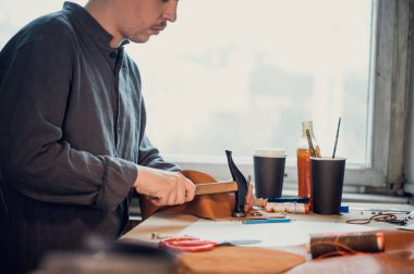 Çekiç kullanan genç bir kunduracı kendi elleriyle yapılan deri bir ürüne perçin düşürür.