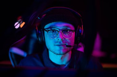 Bilgisayardaki genç bir oyuncunun yakın plan portresi. Kafasında kulaklık olan bir oyun kulaklığı. Neon ışığı. İhracat kavramı.