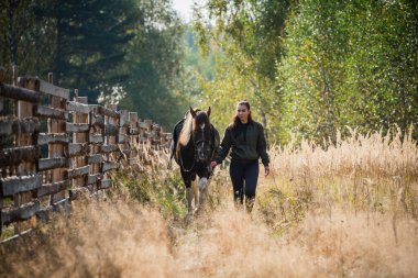 Genç bir kız atına çit boyunca yol boyunca yol gösteriyor.