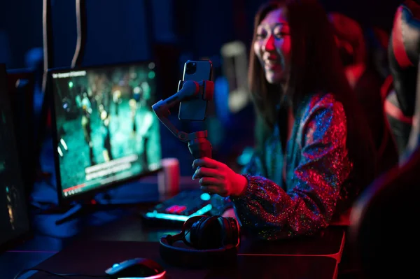 A young asian blogger is streaming from an esports games tournament. Holds a gimbal stabilizer for a smartphone in her hand and takes a selfie. — Stock Photo, Image