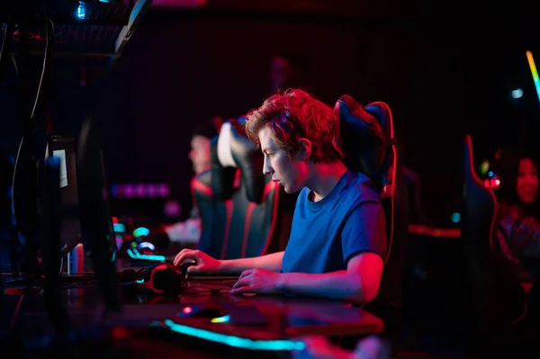 Training bootcamp for professional esports players. Young cyber-athletes play an online shooter game. Glowing keyboard, neon light. — Stock Photo, Image