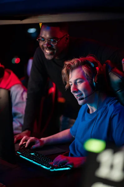 An experienced esports player shows his dark-skinned friend how to play an online video game in a computer club — Stock Photo, Image