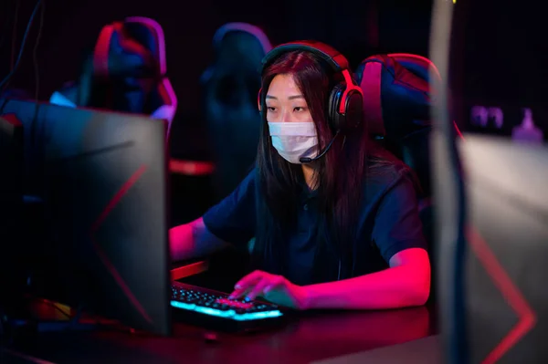 A young asian girl wearing a mask plays online video games in the evening in a computer club — Stock Photo, Image