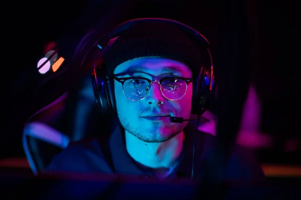 Close-up portrait of a young gamer at the computer. A gaming headset with headphones on the head. Neon light. The concept of esports. — Stock Photo, Image