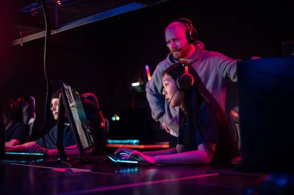A pretty asian woman and a guy spend a date in a computer club, play computer games under the supervision of an experienced esports player — Stock Photo, Image