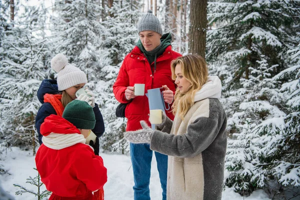 Активная семья с двумя детьми гуляет по их поместью в зимнем снежном лесу за городом и напитки приготовленные горячий кофе из термоса, чтобы сохранить тепло. — стоковое фото