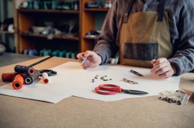 Ayakkabı üretim atölyesinde deneyimli bir ayakkabıcı, farklı aletlerle kağıttan bir ayakkabı modeli yapar.