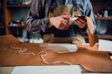 Masadaki atölyesinde genç bir tabakçı deri ayakkabı unsurlarını kesiyor.