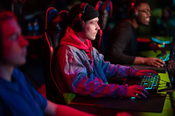 Training bootcamp for professional esports players. Young cyber-athletes play an online shooter game. Glowing keyboard, neon light. — Stock Photo, Image