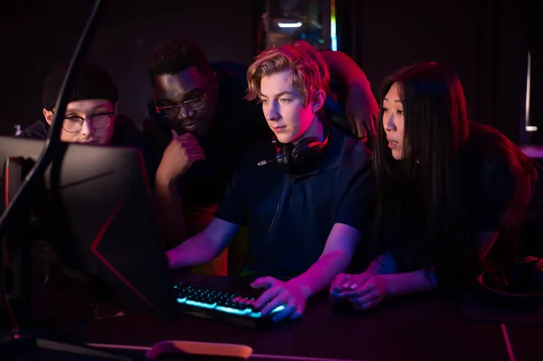 Zwei Jungs und ein Mädchen in medizinischen Masken in einem Computerclub unterstützen ihren Freund bei seinem Spiel — Stockfoto