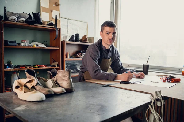 The first stage in the production of shoes is to make an exact pattern from paper, a young shoemaker in uniform at work
