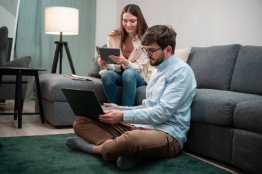 Genç bir kız, evde çalışan sakallı ve gözlüklü erkek arkadaşına yardım ediyor.