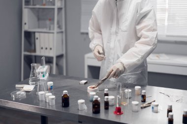 Kimya laboratuvarında çalışan bir bilim adamı. Önplanda kimyasal sıvılar içeren laboratuvar malzemeleri ve cam eşyalar.