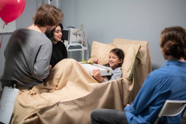 Doğumgünü kızlarını hastanede ziyaret eden hediyeli bir aile.
