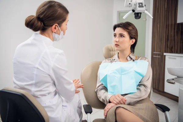 Μια νεαρή γυναίκα να εξηγεί στο γιατρό της τι την ανησυχεί για τα δόντια της. — Φωτογραφία Αρχείου