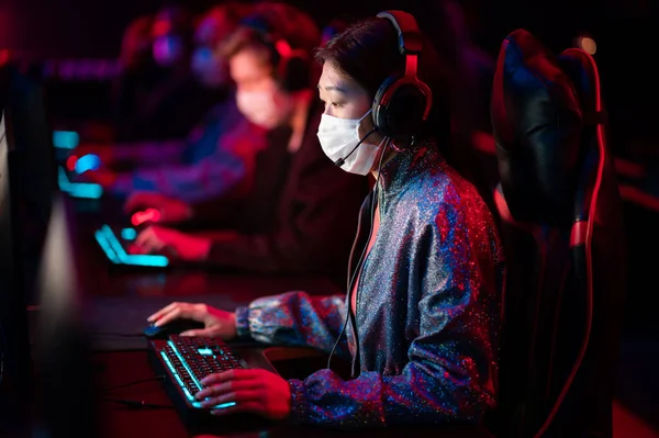 The tournament in the conditions of covid-19 is held in medical masks, gamers play at computers, the team leader is a chinese girl — Stock Photo, Image