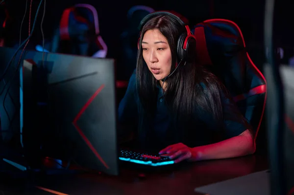 A close-up portrait of a gamer girl wearing headphones in a computer club while playing a game — Stock Photo, Image