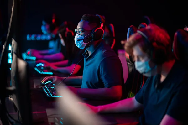 White-skinned and black-skinned guys are members of an esports online strategy crew. Play at the computer at an international tournament during the pandemic. — Stock Photo, Image