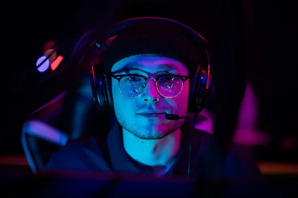 A young cyberathlete wearing glasses and a headset at an esports tournament. Close-up portrait with neon light. — Stock Photo, Image