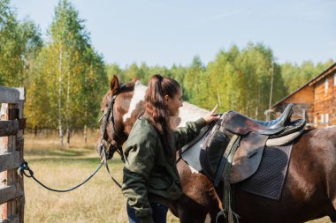 Şirin kız ata binmeye hazırlanır ve bir sonbahar günü eyer takar.