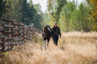 Genç bir at ve binicisi bir kız bir sonbahar günü çitin kenarında birlikte yürüyorlar.