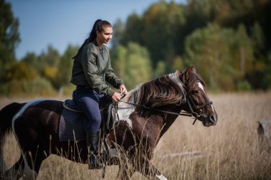 Genç bir kız, şehrin dışında ata binerken sonbahar havasının tadını çıkarıyor.