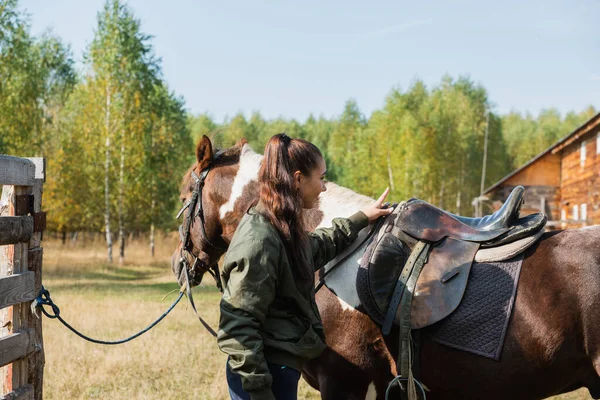 Linda chica se prepara para un paseo en un caballo y lo monta en un día de otoño — Foto de Stock