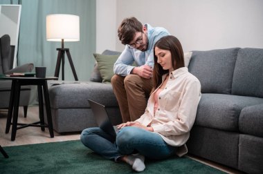 Ev ofisinden zor bir iş gününde, bir kadın iş konusunda bir erkeğe danışır, dizüstü bilgisayarla yerde oturur, adam kanepede yatar.