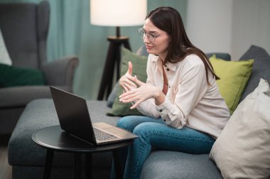 Uzman bir kız uzak bir işte çalışıyor, evinde koltukta oturuyor, yanında bir dizüstü bilgisayar var.