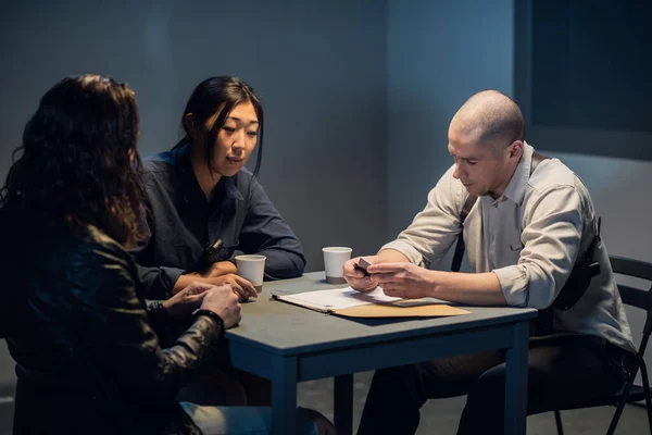 In the interrogation room, the investigator and the officer are talking to the criminal