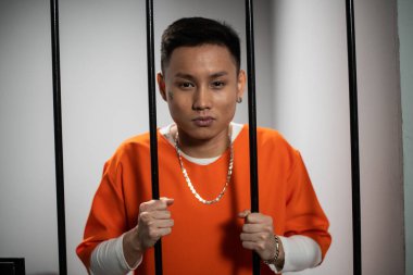 Genç bir Asyalı suçlu hücresindeki parmaklıklara karşı poz veriyor.