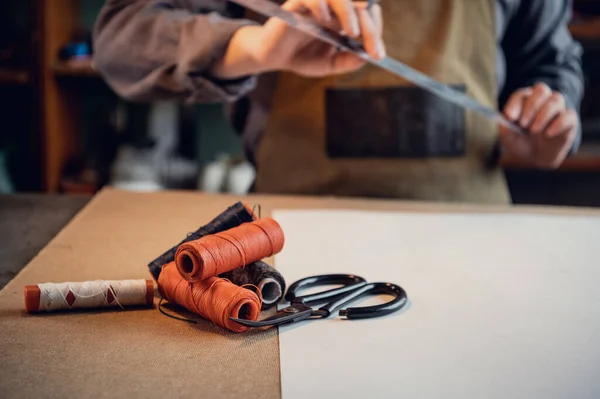 Un zapatero joven hace un dibujo para un patrón de zapatos de cuero en una mesa en su taller — Foto de Stock