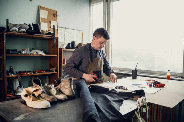 An experienced shoemaker in a shoe production workshop makes a pattern for a shoe from paper with different tools