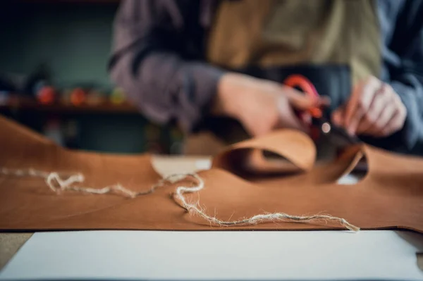 In a boot shop, an experienced young master cuts out leather shoe elements with scissors — Stock Photo, Image