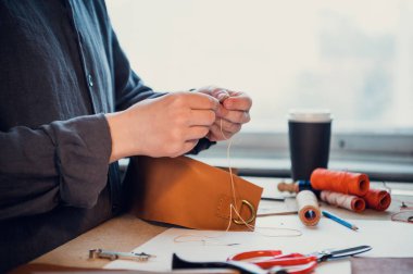 Genç bir kunduracı atölyedeki deri ayakkabılara elle dekoratif öğeler diker.