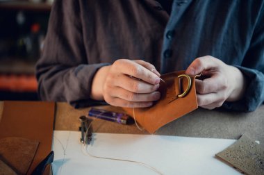 Atölyedeki bir masada oturan genç bir adam elle birbirine deri elementler dikiyor.