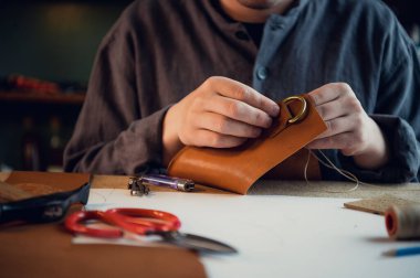 Deneyimli bir tabakçı dikişli deri bir ürün için toka diker.