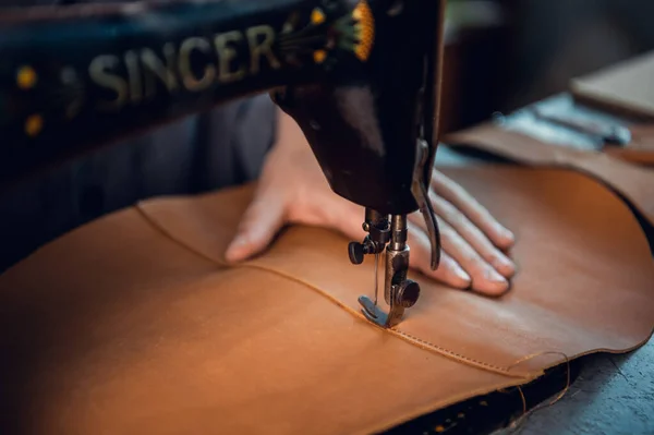 A piece of genuine leather is sewn by a tailor on a sewing machine. Neat seam