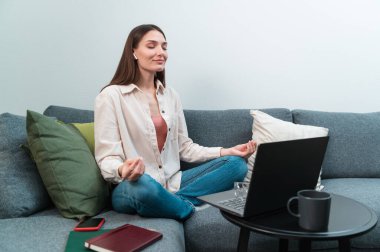 Eski bir yoga koçu ve büyük bir şirketin müdürü çevrimiçi rahatlama eğitimi veriyor, evde dizüstü bilgisayarının önünde Lotus pozisyonunda oturuyor.