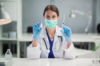 Tıbbi klinikte, Covid-19 'a karşı halkın aşısı başladı. Doktor, üzerinde aşı olan bir şişe gösteriyor.