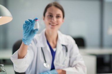 Tıbbi klinikte, Covid-19 'a karşı halkın aşısı başladı. Doktor, üzerinde aşı olan bir şişe gösteriyor.