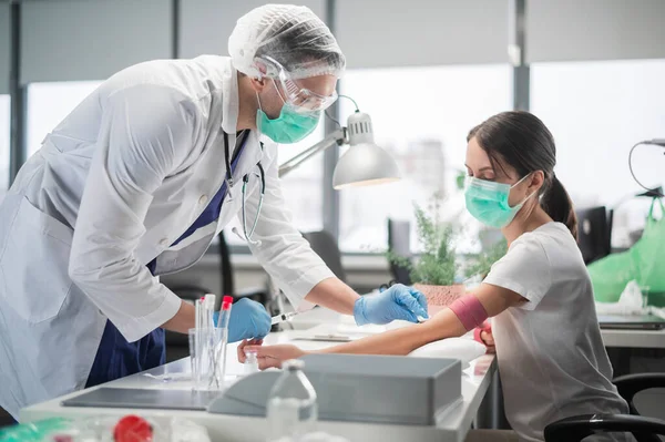 Em uma enfermeira clínica privada um homem coloca um torniquete no braço de uma paciente do sexo feminino e tira sangue de uma veia para análise — Fotografia de Stock